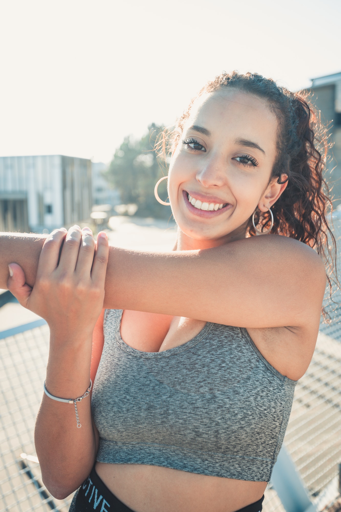 African sports woman standing stretching her arms while smiling to camera urban